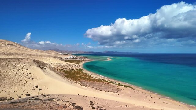 Aerial view of Playa del Matorral with turquoise waters, golden sand dunes, and parked cars under a cloudy sky Canary Islands, Spain.