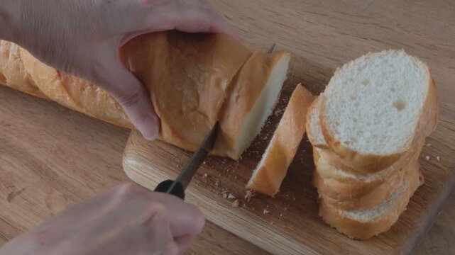 Woman slicing fresh bread with a serrated knife, Woman slicing a loaf of fresh baguette on a wooden board. Close-up of a hand using a serrated knife to slice fresh bread.