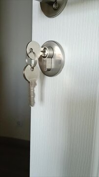 Keys in the metal cylinder lock of a white door close up. Real estate purchase and home safety concept. Key in keyhole.