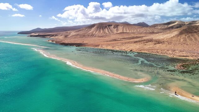 Aerial view of Playa del Matorral with turquoise waters and arid hills under a blue sky in Canary Islands, Spain.