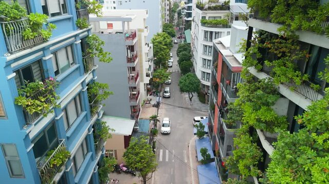 Urban street in southeast asia seen from above, showing density of city life, residential buildings with green balconies, parked cars, and local traffic, creating a calm atmosphere