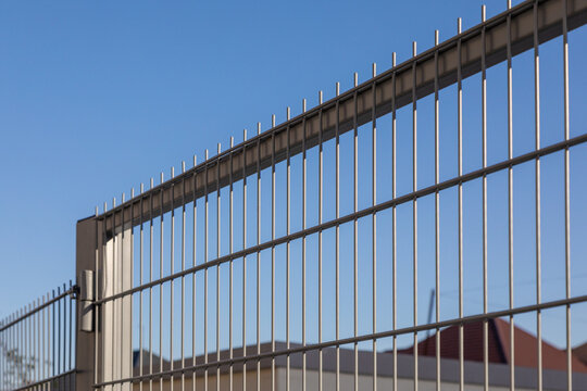 Security infrastructure and urban protection concept. Metal perimeter fence with vertical bars against clear blue sky, minimal industrial architecture detail