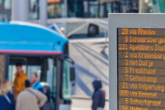 Information panel with Dutch bus departure times in front of  bus with passengers