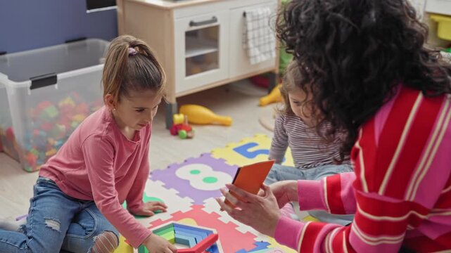 Teacher holds orange flashcard while girl points to colorful puzzle on floor in building; concentration early education play.