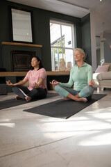 Fototapeta premium Diverse women sitting cross-legged on black yoga mats in living room holding meditative mudra