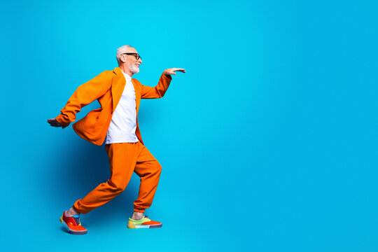 Joyful senior man in orange suit dancing and moving energetically against a bright blue background, fashionable active lifestyle portrait conveying confidence, fun and colorful modern style
