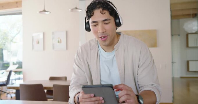 Adult male sitting at wooden table wearing headphones, tapping tablet, glancing left hearing knock