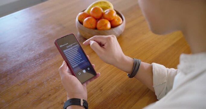 African-American woman holding red phone scrolling list at table with fruit bowl, pausing to decide