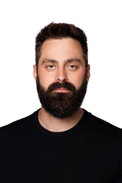 Serious bearded man looking at camera with neutral facial expression. Calm confident young guy posing for ID photo or passport portrait. Brunette male model in black t-shirt on white background