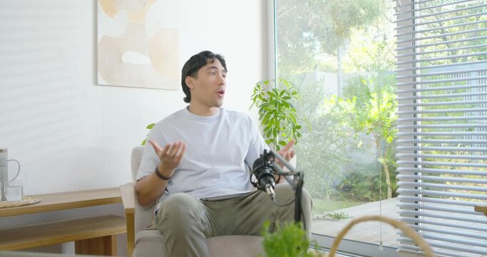 Adult man answering interviewer speaking into microphone gesturing and leaning in armchair at home