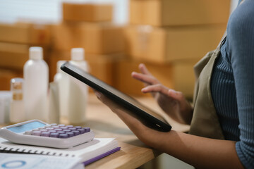 Female ecommerce entrepreneur using tablet to manage online business data and skincare product orders in small business workspace. © Kieng