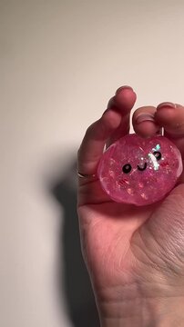 Close-up vertical video of squeezing a shiny pink dumpling squishy toy with one hand, with visible beads inside while pressing, light minimal background, soft lighting.