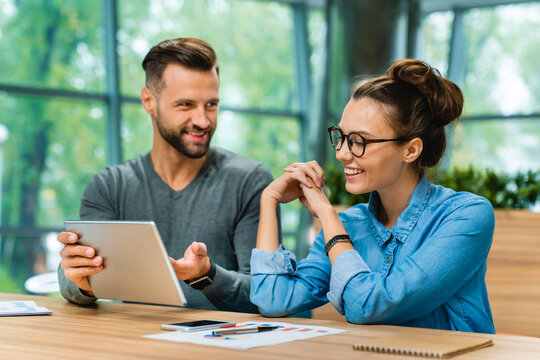 Young man and woman working together with a tablet in a modern office caf&eacute; coworking space, collaborating on tasks and sharing ideas in a dynamic work environment.