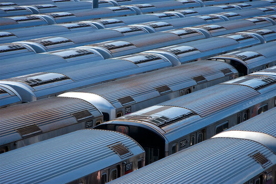 View of subway train cars parked in a rail yard with corrugated metal roofs and side windows New York, New York, United States.