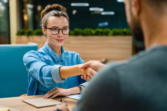 Two young business partners exchanging a handshake in a contemporary office, symbolizing a successful collaboration and partnership in a modern business setting.