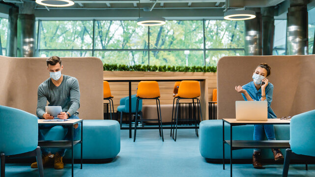 Social distancing concept: Two colleagues maintaining a 1.5-meter distance, wearing medical masks in a modern office, ensuring safety and health protocols while working in a professional environment.