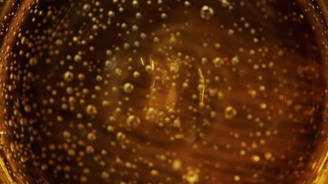 Abstract motion of champagne bubbles forming unique bokeh patterns in a gold liquid texture, captured in a close-up cinematic shot.