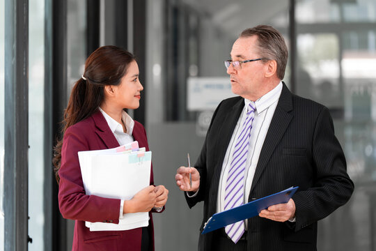 Senior Businessman and Young Asian Woman Discussing Documents in Modern Office
