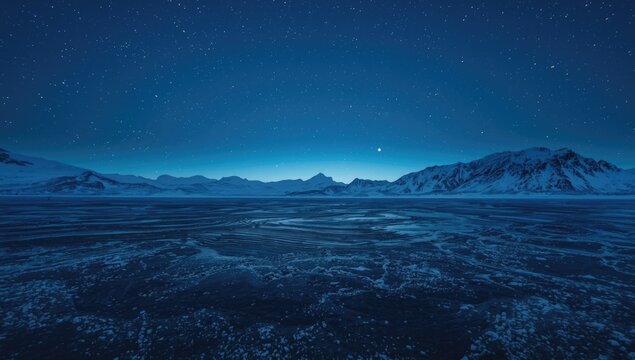 Blue star filled sky over frigid water edge and snow blanketed mountainous horizon