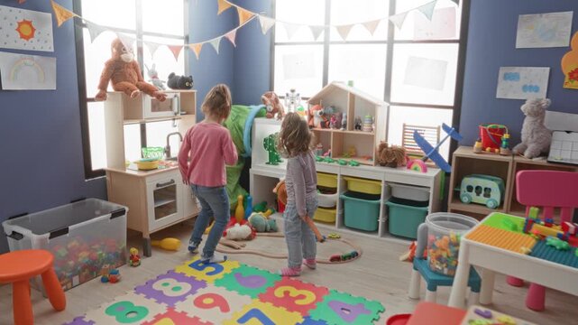 Girl holding a toy horse while another child crouches at a toy kitchen in a colorful playroom inside a building; playful curiosity imagination.