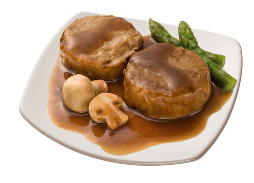 Beef medallion in mushroom sauce with fresh asparagus served on a plate against a white background
