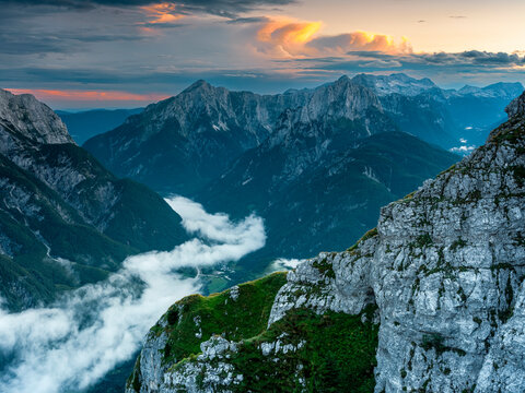 Julian Alps mountain landscape at sunset features rugged peaks rising above a fog-filled valley, offering an adventure travel and tourism destination, Mangart, Italy-Slovenia border.