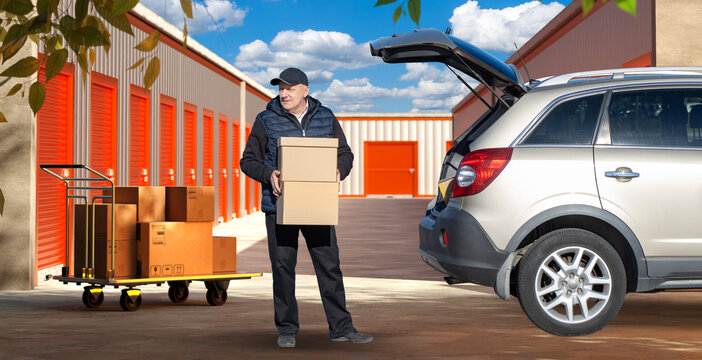 Self storage service. Man carries cardboard boxes from storage unit to car at outdoor self storage facility