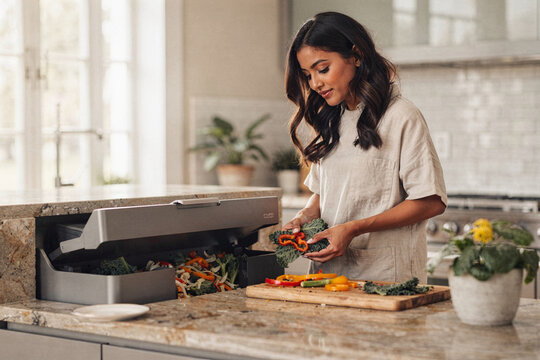 Young woman disposing of vegetable scraps into a modern built-in kitchen composter for sustainable living