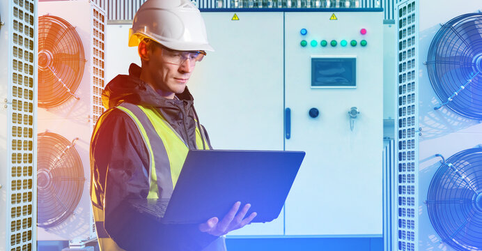 HVAC maintenance. Engineer checks industrial cooling equipment with laptop in mechanical room between ventilation units