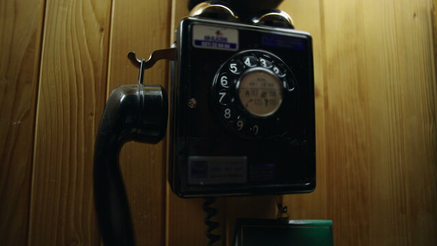 Hand lifting and returning receiver of vintage rotary wall telephone inside wooden chalet interior, retro communication gesture on rustic paneling
