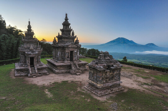 View of the ancient stone structures of Gedong Songo Temple with mountain peaks in the distance under a soft morning sky Bandungan, Jawa Tengah, Indonesia.