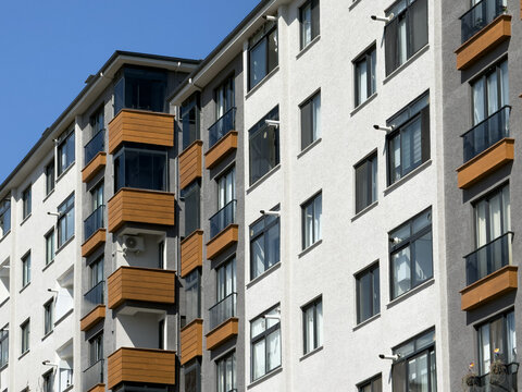 View of modern residential apartment building facade with wooden balcony accents and glass windows under a clear blue sky in Avcilar, Istanbul, Turkiye.