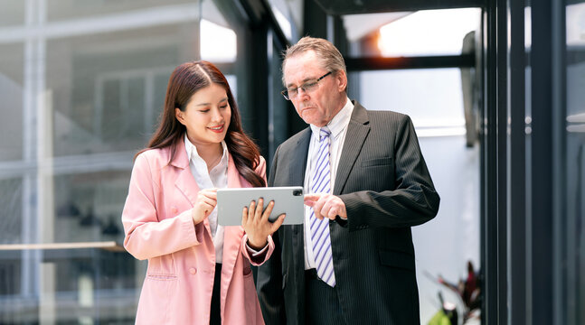 Young Asian Businesswoman and Senior Colleague Looking at Tablet in Modern Office