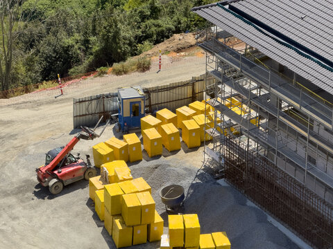 View of a construction site featuring a red telehandler, stacks of yellow insulation blocks, and scaffolding against a building under construction in Avcilar, Istanbul, Turkiye.