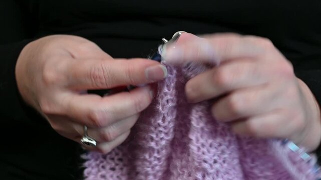 Hands knitting pink wool yarn, metal needles working loops.