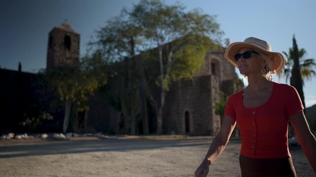 Mature woman walks near Mission Church Santa Rosalia in Mulege, Baja California, discovering the area with palm trees and mountains