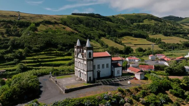 Cinematic Aerial Drone Shot of a Historic Baroque-Style Church with Twin Spires Nestled Against Lush Green Terraced Slopes, Flores Island