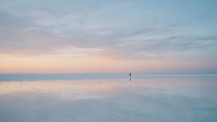 Fototapeta premium Silhouette Person Walking on Vast Pastel Salt Flat at Dusk Toward Freedom Perfect for Wellness Advertising Corporate Vision and Travel Campaign