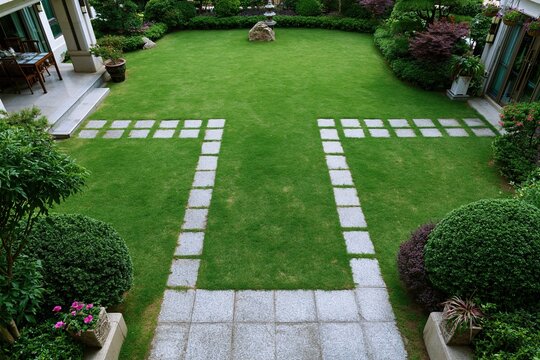 Neat well maintained private residential backyard garden with bright green lawn and gray stone stepping path flanked by trimmed bushes and colorful flowering plants