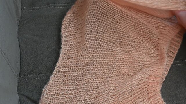 Knitted peach shawl held by hands, soft wool fabric texture, light orange yarn.