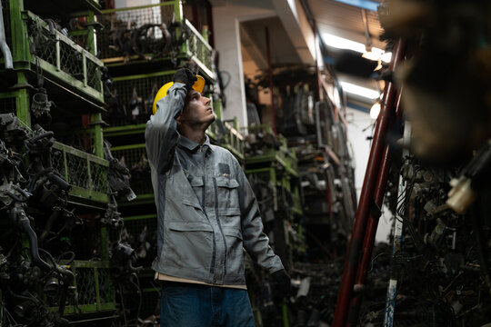 Busy worker inspects parts on shelf in auto junkyard
