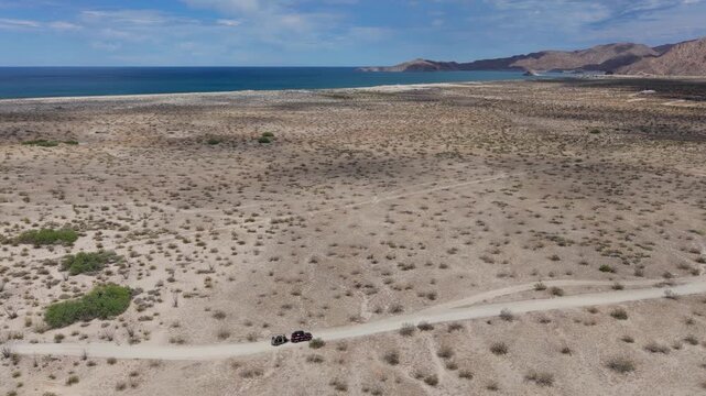 An SUV pulls away from a dispersed campsite by the Sea of Cortez in Baja California, Mexico, towing a teardrop camper trailer.