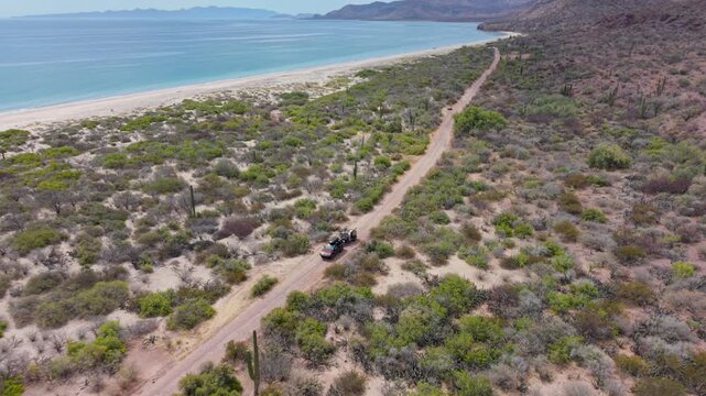 An SUV pulls a teardrop camper trailer from a campsite at the beach in Mulege Baja California Sur, surrounded by desert and mountains.