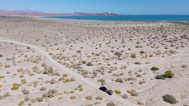 Aerial views show SUV with teardrop camper trailer traveling on dirt roads by the ocean in Baja California during camping trip.