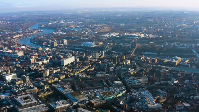 4K aerial view of Newcastle upon Tyne city centre with the iconic Tyne Bridge, Gateshead Millennium Bridge, Sage music venue and meandering River Tyne under winter haze.