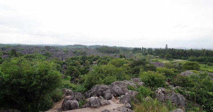 Camera pushes forward from inside observation deck pavilion to reveal panoramic view of Shilin Stone Forest, Yunnan. Simple architectural stone pillars of gazebo frame vast landscape