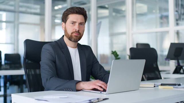 Concentrated 40s Caucasian middle-aged business man working online with laptop technology looking at camera with serious expression mature businessman work with computer cyberspace male in office