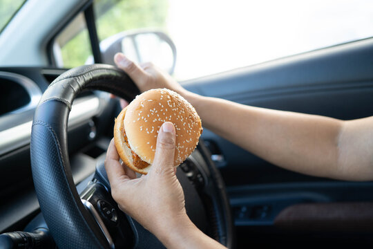 Asian woman driver hold and eat hamburger in car, dangerous and risk an accident.