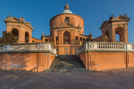 View of Santuario Madonna di San Luca with its terracotta facade, symmetrical porticos, and stone steps under a clear blue sky Bologna, Emilia-Romagna, Italy.