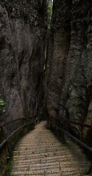 Very steep stone stairway leads to bottom of deep, narrow canyon in famous Shilin Stone Forest. Vertical POV shot of cautious descent down ribbed steps, hemmed in by massive, scabrous karst walls.
